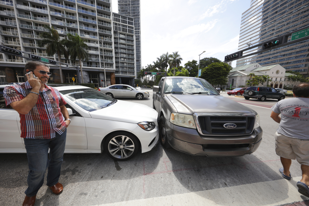 A man stands beside a damaged car after a collision, indicating a car accident scene in Miami.