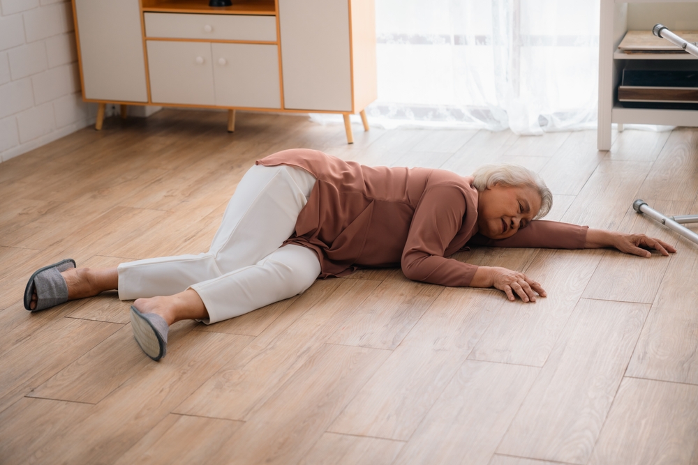 An elderly woman lying on the floor in a room, possibly after a slip and fall injury.