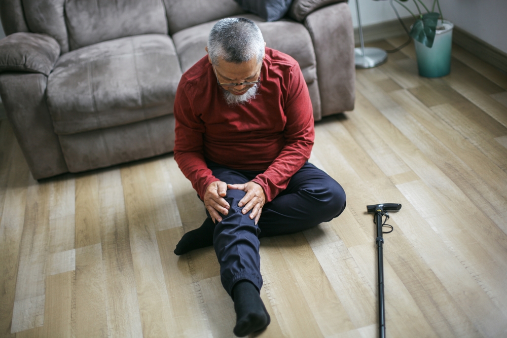A man seated on the floor, visibly in pain, with his hand on his knee, related to a slip and fall injury evaluation