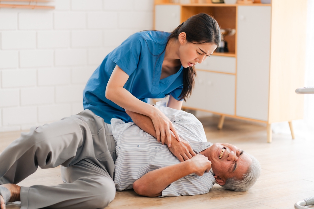 A woman assists an elderly man who has fallen on the floor, likely providing medical help after a slip and fall incident.