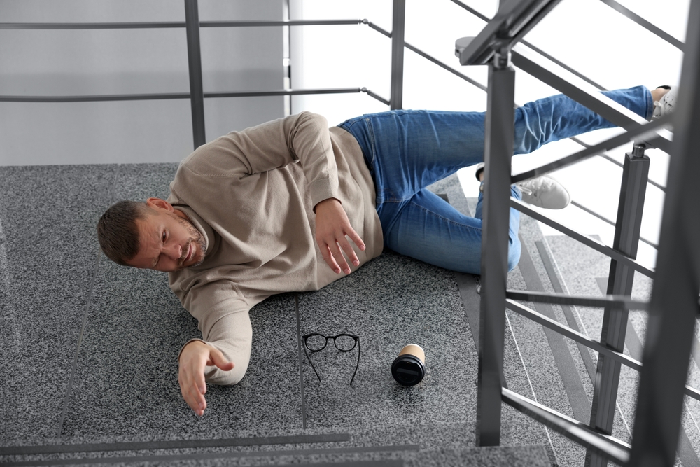 A man sprawled on the floor, hands out, as part of his recovery from a slip and fall injury with orthopaedic support.