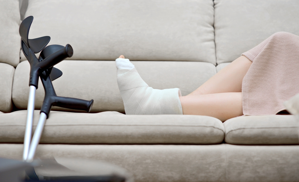 A woman sitting on a couch with a cast on her leg, resting after treatment for fall injuries.